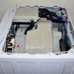 A top view of an open front load washing machine, from the side, awaiting to be serviced.