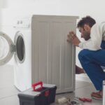Repairman fixing a washing machine, he is adjusting a knob, professional service concept