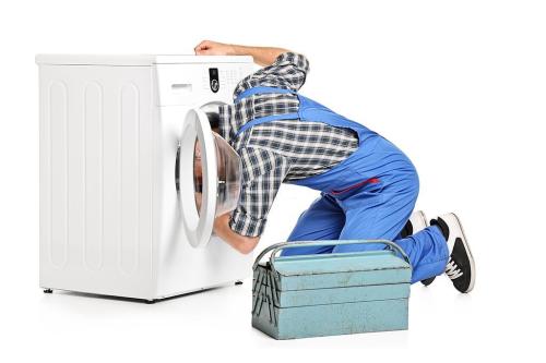 A repairman trying to fix a washing machine isolated on white background